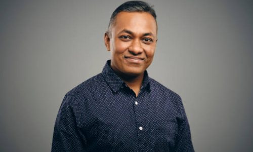 A studio portrait of an Indian man against a brown background.